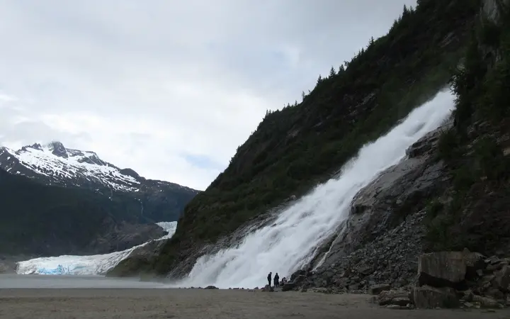 Nugget Falls cascading down a cliff beside Mendenhall Lake, with Mendenhall Glacier in the background
