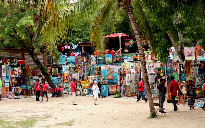 Colourful Haitian paintings displayed under palm trees at the Labadee Artisan's Market