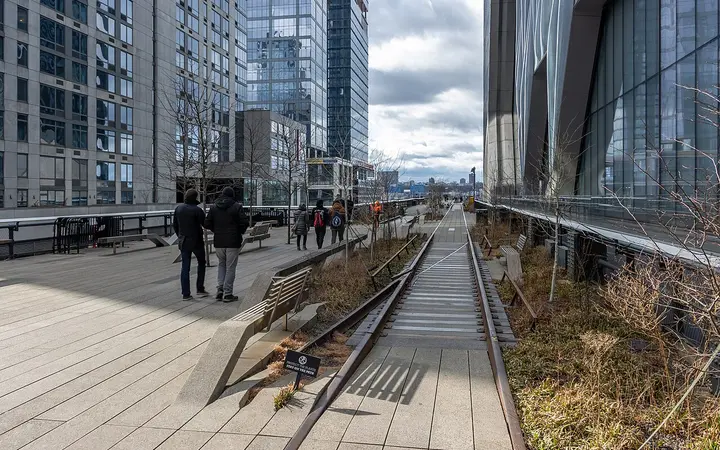 Walkers on the High Line beside preserved rail tracks and tall buildings at Hudson Yards