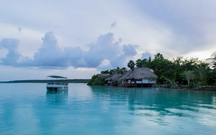 Turquoise water of Bacalar Lagoon with a pontoon boat and a thatched waterfront building