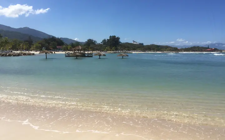 Calm turquoise water and white sand at a Labadee beach with palm trees and hills behind