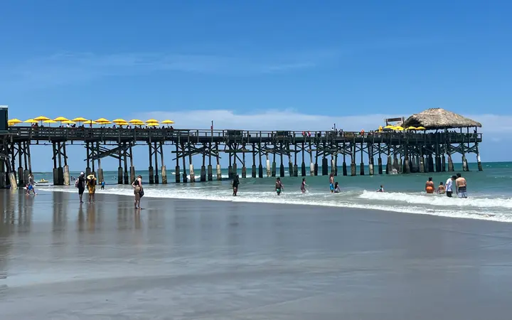 Cocoa Beach Pier seen from the beach, with swimmers in the surf and yellow umbrellas on the pier