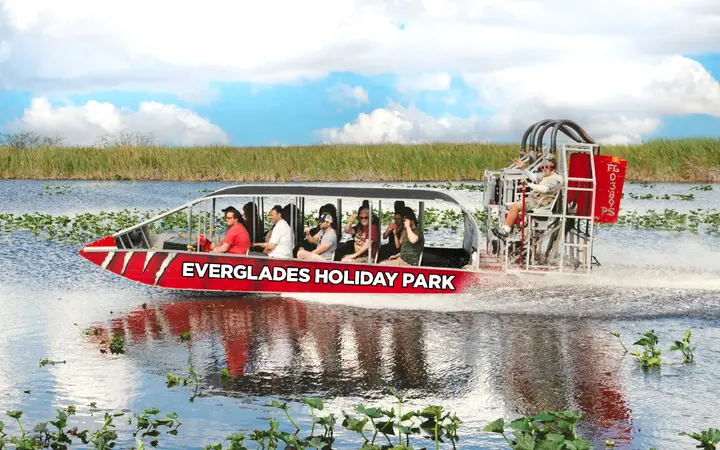 A red Everglades Holiday Park airboat carrying passengers across the Everglades marsh