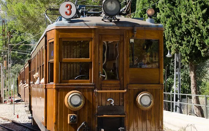 Wooden Sóller railway train arriving at Bunyola station among pine trees