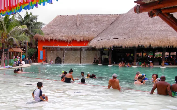 Cruise passengers in the large saltwater pool with a thatched swim-up bar inside the Puerto Costa Maya port complex