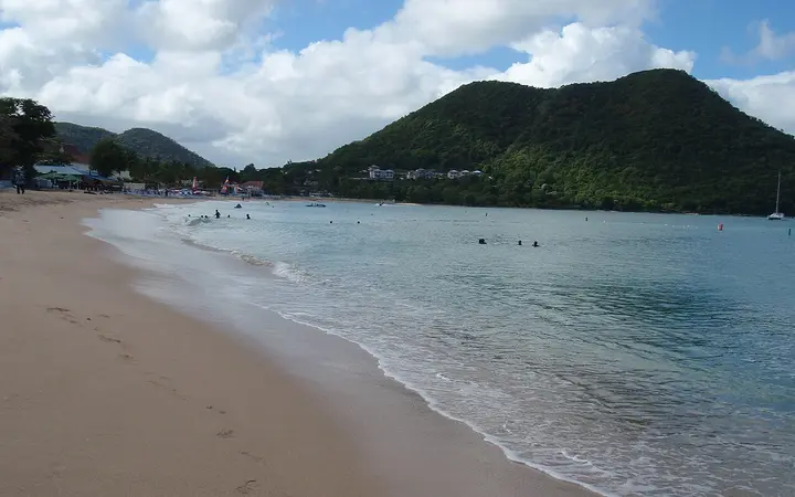 Golden sand and calm turquoise water at Reduit Beach, Rodney Bay, with a green hill behind