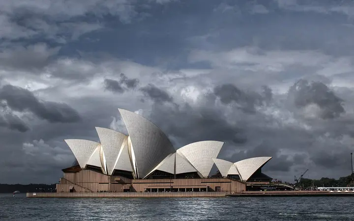 Sydney Opera House sails under a cloudy sky seen across the harbour