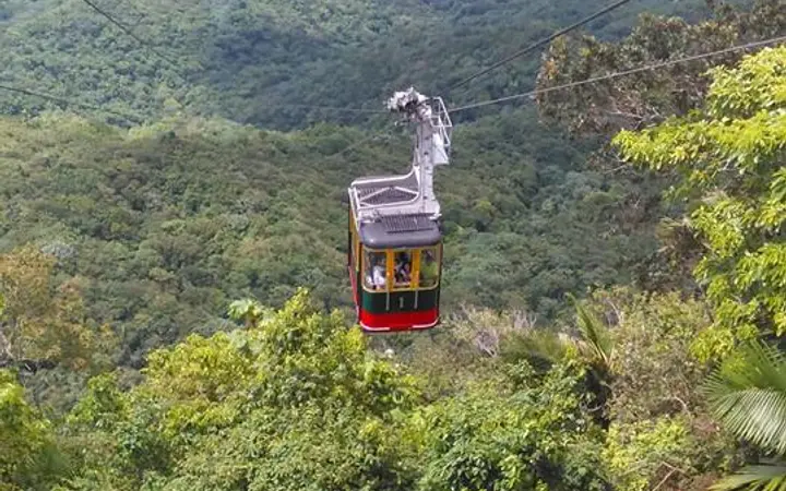 Red cable car cabin above forest with Puerto Plata city and coast below