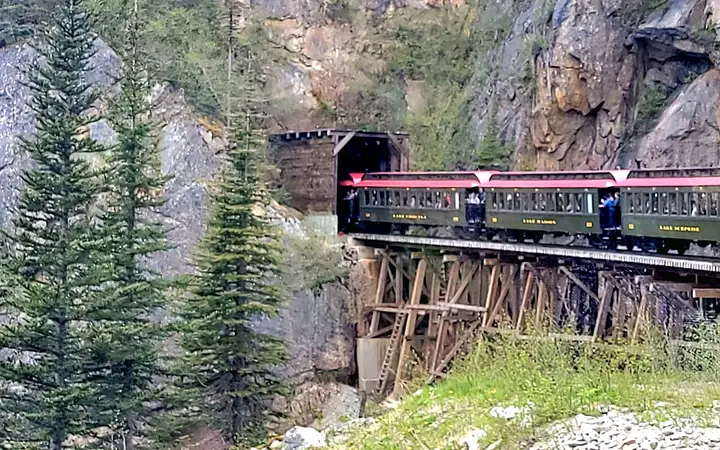 White Pass and Yukon Route passenger train crossing a wooden trestle into a rock tunnel north of Skagway