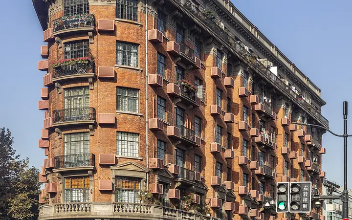 Wukang Mansion, a wedge-shaped 1920s brick apartment building on a corner of Wukang Road under a blue sky