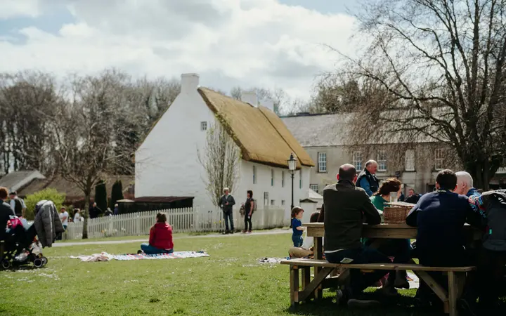 Visitors picnicking in the grounds of the Ulster Folk Museum beside a thatched cottage