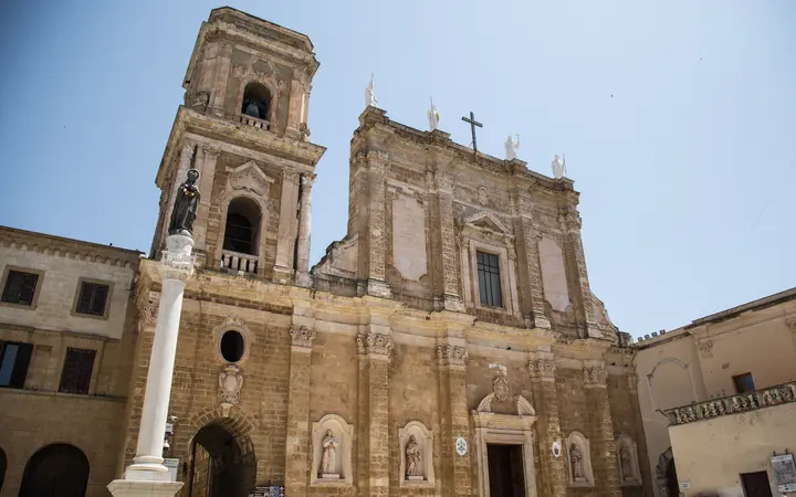 Baroque facade and bell tower of Brindisi Cathedral on Piazza Duomo, with a white column in front, under a clear sky