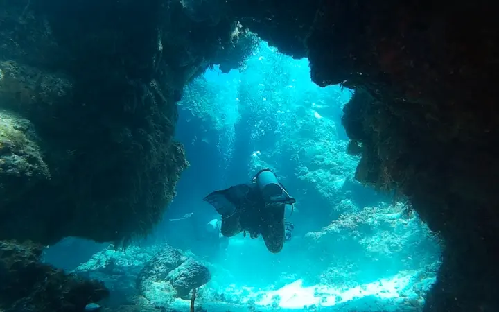Diver swimming through a coral swim-through on Palancar Reef, Cozumel