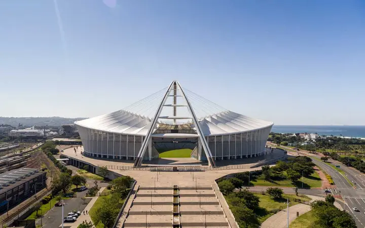 Moses Mabhida Stadium's white bowl and tall arch near the beachfront under a blue sky