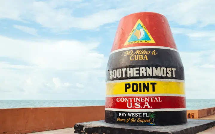 The red, black and yellow Southernmost Point buoy in Key West, against a blue sky and the sea