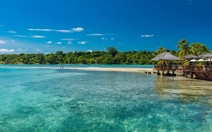 Clear turquoise water of Erakor Lagoon with a palm-fringed shore and overwater buildings near Port Vila