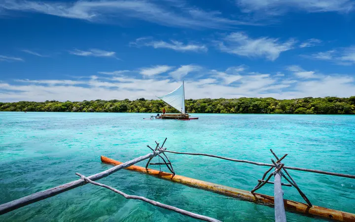 Traditional sailing pirogue on the turquoise water of Upi Bay.