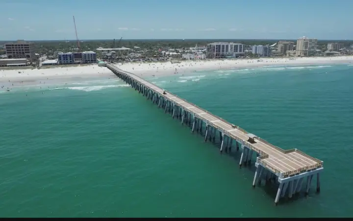 Aerial view of a long fishing pier reaching into green-blue Atlantic water off Jacksonville's beaches