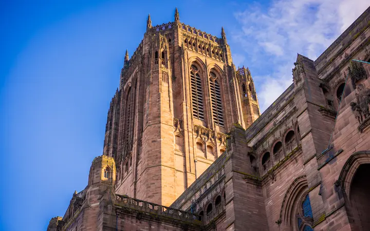The sandstone central tower of Liverpool Cathedral seen from below against a blue sky with light cloud