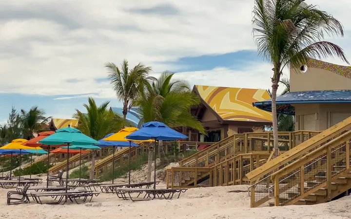 Beach cabanas with umbrellas and wooden stairs among palm trees at Mabrika Cove, Disney Lookout Cay