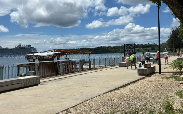 Paved seafront promenade along Port Vila harbour on a sunny day, with a cruise ship far in the background