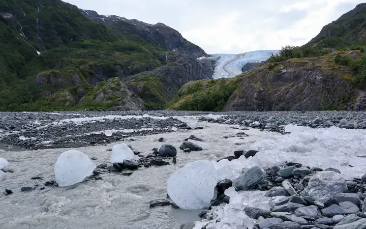 Exit Glacier at the head of its valley, with grey glacial boulders and chunks of ice in the outwash plain in front