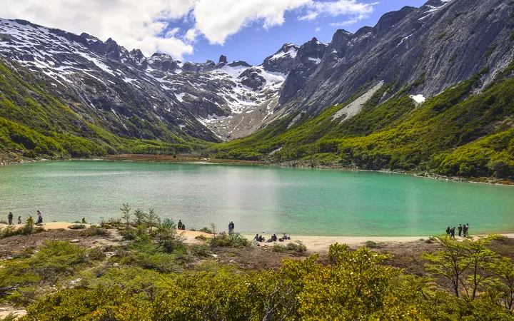 The turquoise waters of Laguna Esmeralda below green slopes and snow-streaked peaks.