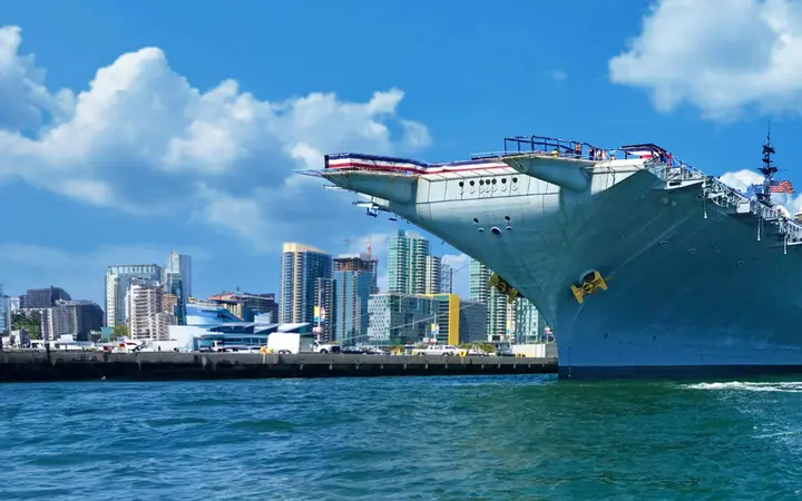 The aircraft carrier USS Midway moored on San Diego Bay with the downtown San Diego skyline behind it on a sunny day