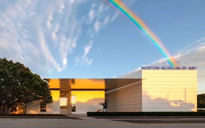 The Norton Museum of Art's modern facade and banyan tree under a blue sky with a rainbow.