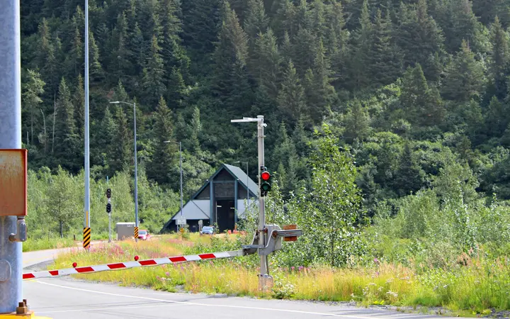 Portal of the Anton Anderson Memorial Tunnel with its traffic signals and gate, set against a forested mountainside